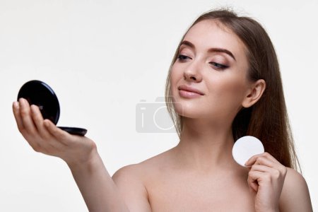 Photo for Beautiful young woman look at mirror and holding white cotton pad on white background - Royalty Free Image