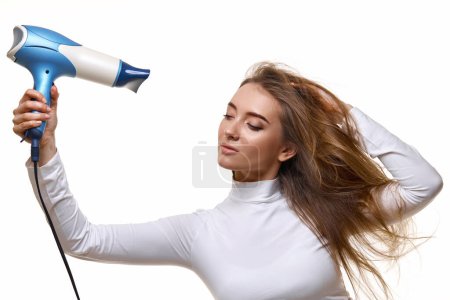 Téléchargez les photos : Belle jeune femme séchage forte cheveux sains avec sèche-cheveux i isolé sur fond blanc - en image libre de droit