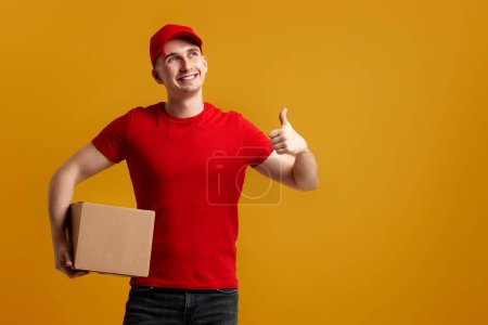 Foto de Empleado del repartidor en gorra roja, camiseta roja con caja de cartón aislada sobre fondo amarillo - Imagen libre de derechos