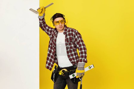 Photo for Worker man or builder in construction helmet near white banner on yellow background. building carpentry profession - Royalty Free Image