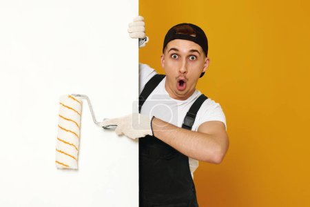 Photo for Surprised young man in working clothes painting white walls in the room. copy space for text - Royalty Free Image
