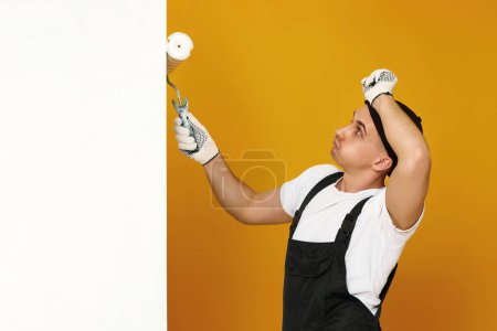 Photo for Tired man in working clothes work with paint roller, wall painting, web banner and copy space - Royalty Free Image