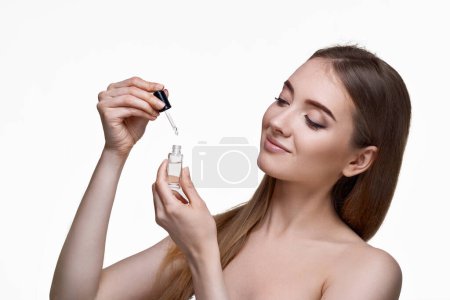 Téléchargez les photos : Belle femme tenant bouteille avec sérum pour les soins de la peau sur fond blanc - en image libre de droit