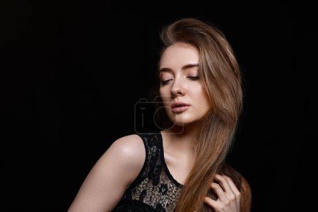 Téléchargez les photos : Magnifique femme brune aux cheveux longs en robe noire sur fond noir. espace de copie - en image libre de droit