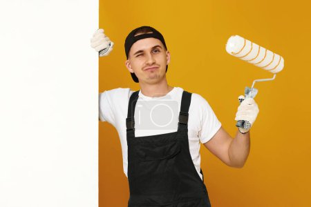 Photo for Young man in working clothes painting white walls in the room. copy space for text - Royalty Free Image