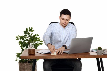Photo for Businessman in blue shirt taking notes, using laptop computer on white background - Royalty Free Image