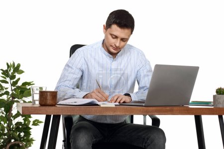 Photo for Businessman in blue shirt taking notes, using laptop computer on white background - Royalty Free Image