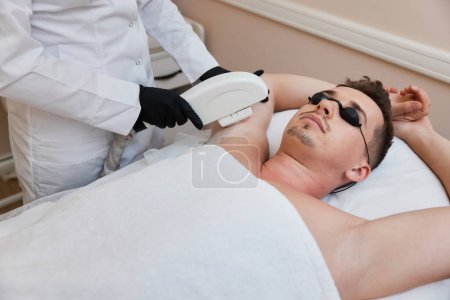 Photo for Young man receiving epilation in beauty center. Professional beautician doing laser hair removal procedure on male face. - Royalty Free Image