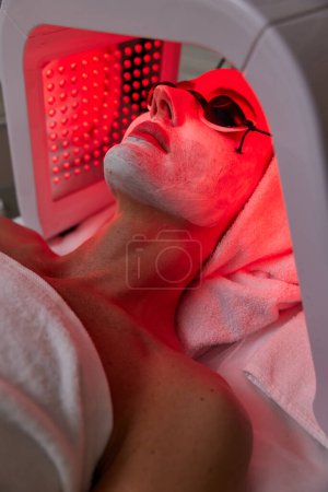 Téléchargez les photos : Femme dans des lunettes de protection obtenir un traitement facial avec thérapie led. Masque LED à la clinique de beauté - en image libre de droit