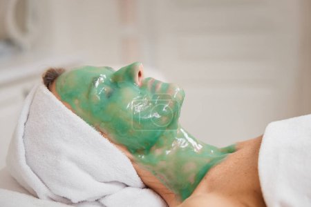 Foto de Hermosa mujer con máscara de alginato verde en la cara en el salón de spa. primer plano - Imagen libre de derechos