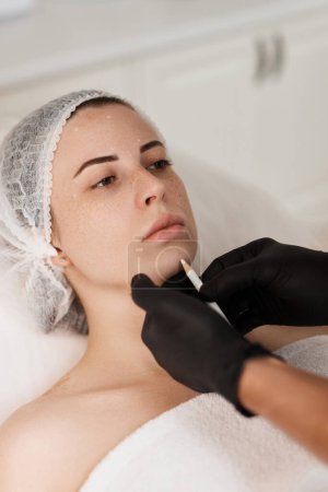 Foto de Cosmetólogo masculino marcando la piel de la mujer caucásica con lápiz blanco. marcado facial para el procedimiento estético. - Imagen libre de derechos