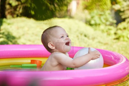 Foto de Chica linda feliz del bebé con la bola en piscina inflable del cabrito en el jardín. Temporada de verano - Imagen libre de derechos