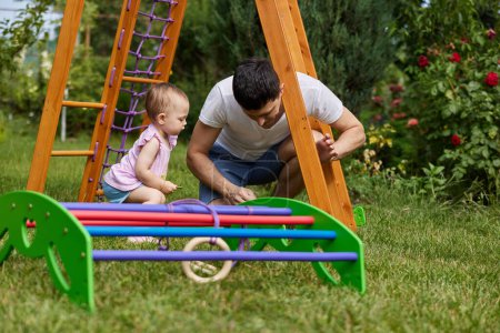 Téléchargez les photos : Papa avec petite fille enfant fille recueille en bois maison complexe sportif en plein air. processus d'assemblage - en image libre de droit