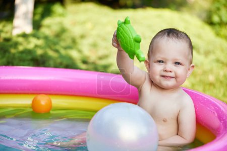 Foto de Feliz niña linda jugando con la bola en la piscina inflable del niño en el jardín. Temporada de verano - Imagen libre de derechos