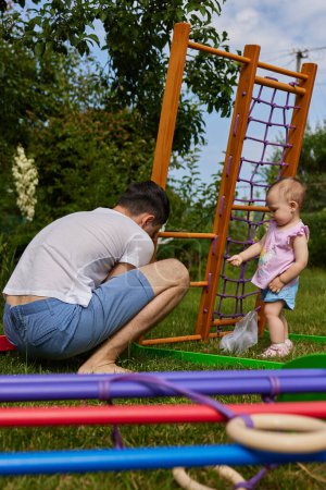 Téléchargez les photos : Petite fille enfant fille aide son père à recueillir en bois complexe sportif en plein air. processus d'assemblage - en image libre de droit
