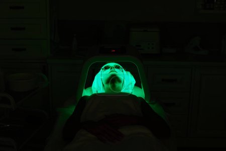 Foto de Mujer con gafas protectoras recibiendo tratamiento facial con terapia dirigida. Máscara led en la clínica de belleza - Imagen libre de derechos