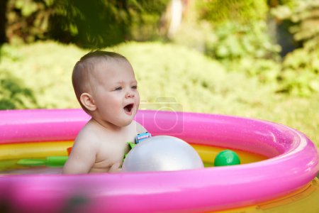 Foto de Chica linda excitada del bebé con la bola en piscina inflable del cabrito en el jardín. Temporada de verano - Imagen libre de derechos