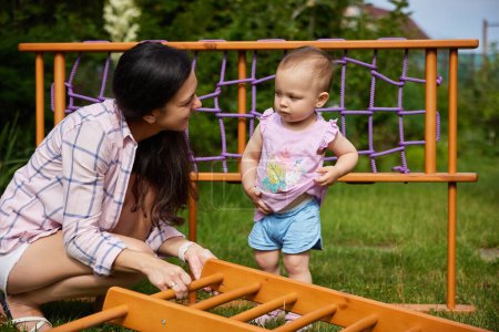 Téléchargez les photos : Mère avec petite fille enfant fille recueille en bois maison complexe sportif en plein air. processus d'assemblage - en image libre de droit