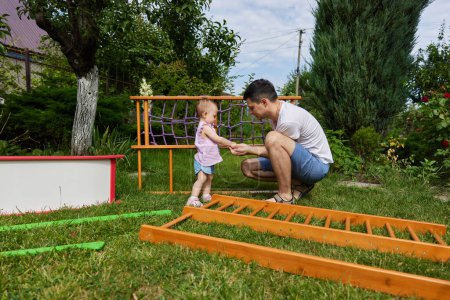Téléchargez les photos : Papa avec petite fille enfant fille recueille en bois maison complexe sportif en plein air dans la journée d'été - en image libre de droit