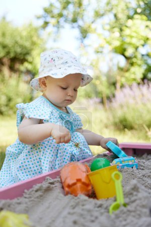 Foto de Linda niña jugando en arena en caja de arena con varios juguetes en el patio al aire libre - Imagen libre de derechos