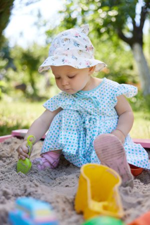 Foto de Linda niña jugando en arena en caja de arena con varios juguetes en el patio al aire libre - Imagen libre de derechos