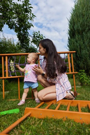 Photo for Mother with little child girl daughter collects wooden home sports complex outdoor. assembly process - Royalty Free Image
