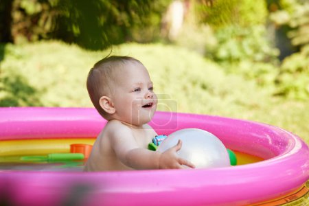 Photo for Happy cute baby girl with ball in kid inflatable pool in the garden - Royalty Free Image