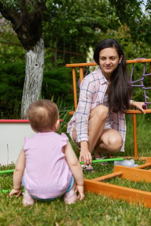 Téléchargez les photos : Mère avec petite fille enfant fille recueille en bois maison complexe sportif en plein air. processus d'assemblage - en image libre de droit