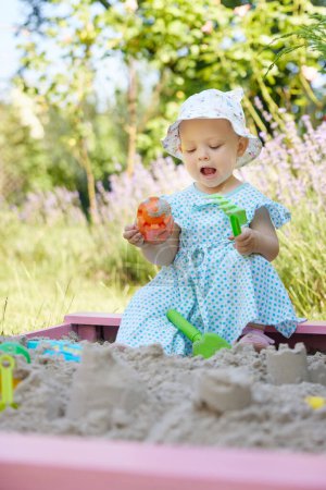 Téléchargez les photos : Mignonne petite fille jouant dans le sable dans un bac à sable avec divers jouets sur aire de jeux extérieure - en image libre de droit