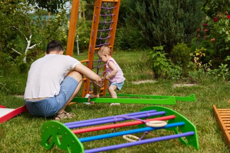 Foto de Niña pequeña hija ayuda a su padre a recoger complejo deportivo de madera al aire libre. proceso de montaje - Imagen libre de derechos