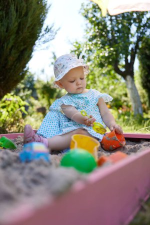 Photo for Cute little girl playing in sand in sandbox with various toys on outdoor playground - Royalty Free Image