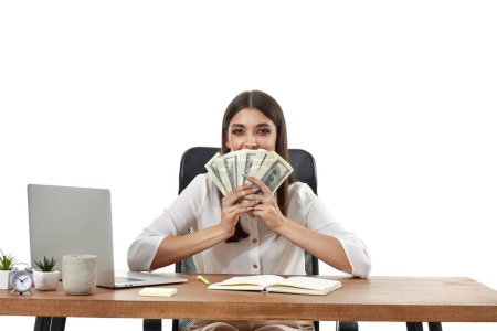 Téléchargez les photos : Belle femme d'affaires travaillant sur ordinateur portable et tenant de l'argent sur le visage - en image libre de droit