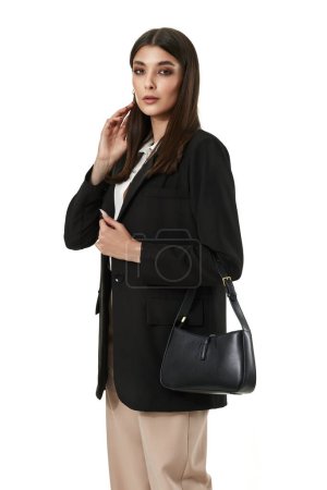 Téléchargez les photos : Belle femme avec sac en cuir en blazer noir et pantalon beige isolé sur fond blanc - en image libre de droit