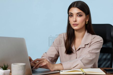 Téléchargez les photos : Belle femme d'affaires élégante en utilisant un ordinateur portable pour le travail en ligne à table et en regardant la caméra - en image libre de droit