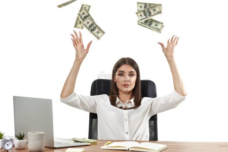 Téléchargez les photos : Femme d'affaires travaillant sur un ordinateur portable et jetant de l'argent tout en étant assis sur une chaise au bureau. les billets volent dans les airs - en image libre de droit