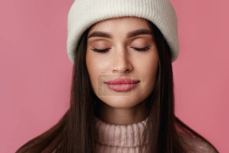 Foto de Retrato de mujer joven en sombrero blanco, suéter rosa perder los ojos en el placer sobre fondo rosa pastel. - Imagen libre de derechos