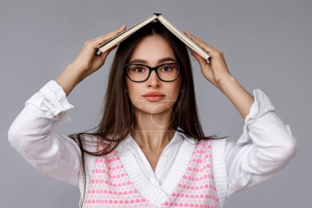 Photo for Pretty brunette woman in glasses with book on head on grey background - Royalty Free Image