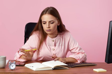 Téléchargez les photos : Belle gestionnaire féminin en utilisant un ordinateur PC pour le travail en ligne sur fond rose - en image libre de droit