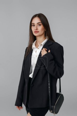 Téléchargez les photos : Belle femme avec sac à main en blazer noir isolé sur fond gris - en image libre de droit