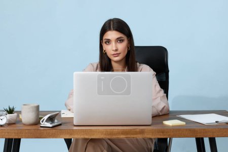 Téléchargez les photos : Belle gestionnaire féminin en utilisant un ordinateur portable pour le travail en ligne à table sur fond beige - en image libre de droit
