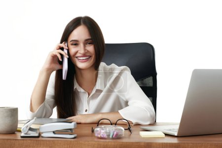 Photo for Emotional businesswoman working with laptop and having phone conversation in the office - Royalty Free Image