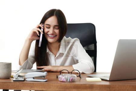 Téléchargez les photos : Belle femme gestionnaire d'entreprise travaillant avec ordinateur portable et avoir une conversation téléphonique dans le bureau - en image libre de droit
