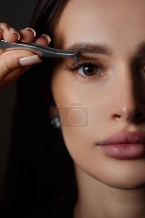 Photo for Beauty professional woman holding eyelash tweezers while posing on black background. close-up - Royalty Free Image