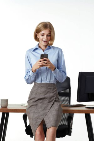 Téléchargez les photos : Heureux excité blonde femme d'affaires en utilisant le téléphone intelligent dans le bureau - en image libre de droit