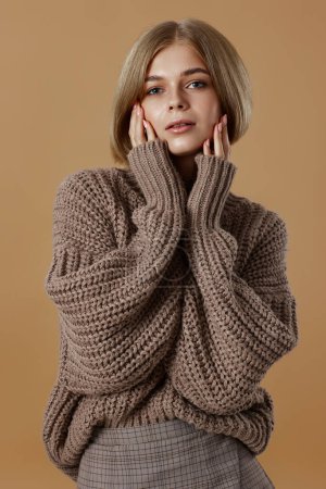 Photo for Beautiful blonde woman in brown knitted sweater on beige background. autumn style - Royalty Free Image