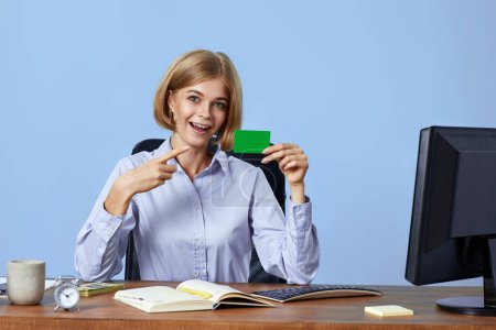 Foto de Atractiva mujer de negocios rubia apuntando a la tarjeta de crédito de plástico sobre fondo azul - Imagen libre de derechos