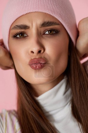 Foto de Retrato de mujer juguetona con labios enfurecidos en sombrero rosa sobre fondo rosa pastel. primer plano - Imagen libre de derechos