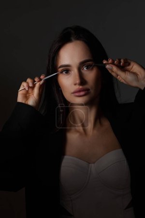 Photo for Beauty professional woman holding tweezers while posing on black background - Royalty Free Image