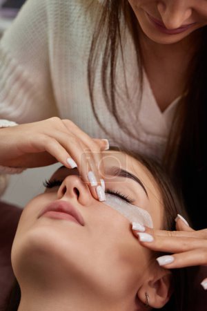 Photo for Cosmetologist preparing glue ribbon under eye. Eyelash extension procedure - Royalty Free Image