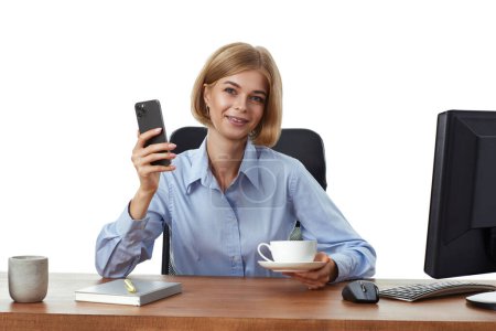 Foto de Mujer de negocios rubia positiva usando el teléfono, beber café en la oficina - Imagen libre de derechos
